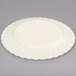A Fineline Flairware ivory plastic plate with a wavy design on a gray surface.