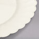 A Fineline Flairware ivory plastic plate with a scalloped edge on a white surface.
