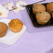 A plate of muffins on a luscious lavender table cover.