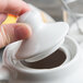 A person's hand holding a white Tuxton teapot lid.