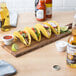 A Tablecraft acacia wood paddle serving board with tacos and drinks on a table.