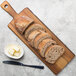 A Tablecraft acacia wood serving board with sliced bread next to butter and a knife.