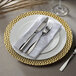A white plate with a gold hammered rim on a white background with silverware and a napkin on it.