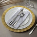 A white plate with a gold geometric design on the rim with silverware on a white napkin.