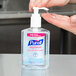 A person using a pump dispenser to use Purell hand sanitizer.