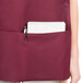A woman wearing a burgundy Intedge cobbler apron with a notebook and pen in the pocket.