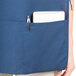A person wearing a navy blue Intedge cobbler apron with a pen and notebook in the pockets.