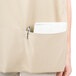A woman wearing a beige Intedge cobbler apron with a pen and notebook in the pocket.