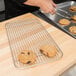 A person using a Vollrath stainless steel wire pan grate to cool chocolate chip cookies.