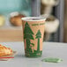 A close-up of a EcoChoice Kraft paper hot cup with a tree print on a table with a cup of coffee and a croissant.