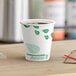 A close-up of a EcoChoice paper hot cup with green leaves on it filled with coffee.