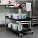 A black Rubbermaid three-shelf utility cart with white buckets on it.