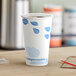 A white EcoChoice paper hot cup with blue leaf print on a table.