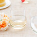 A clear plastic stemless wine goblet filled with white wine on a table next to a yellow and white pastry.