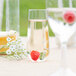 A clear plastic stemless flute filled with a champagne and a raspberry.