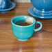 A turquoise Fiesta china cup filled with tea and a tea bag on a table.