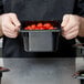 A person holding a Cambro black polycarbonate food pan full of tomatoes.