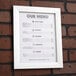 A white Aarco snap frame holding a menu on a brick wall.
