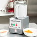 A Robot Coupe food processor with a bowl of orange food inside.