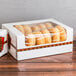 A 10 pack of white auto-popup window bakery boxes with a printed graphic holding donuts on a table.