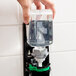 A hand holding a bottle of GOJO Clear & Mild foam hand soap in front of a wall mounted soap dispenser.