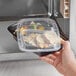 A hand holding a Choice black plastic rectangular 2-compartment container filled with food.