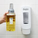 A hand holding a GOJO Citrus Ginger foam soap bottle next to a white soap dispenser with a hole.
