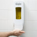 A person pressing the yellow GOJO hand soap dispenser.