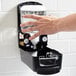 A hand reaching out to touch a GOJO chrome touchless hand soap dispenser.