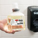 A hand holding a clear bottle of GOJO E2 foam hand soap with PCMX.