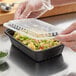 A person in gloves using a Choice black rectangular microwavable heavy weight container and lid to store food.
