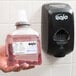 A hand holding a plastic bottle of GOJO Premium Foam Hand Soap next to a hand soap dispenser.