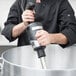A chef using a Waring Big Stik immersion blender to mix a large pot in a professional kitchen.