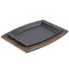 A rectangular black tray on a wooden surface with a Lodge UCPU rectangular wood underliner.