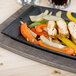 A Lodge rectangular cast iron fajita skillet with chicken, peppers and onions on a table.