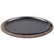 A round black cast iron pan on a Lodge oval wood underliner with walnut finish.