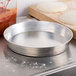 An American Metalcraft aluminum pizza pan with dough on it on a counter.