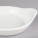 A CAC bone white stoneware shirred egg dish with a handle on a gray surface.