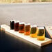 A Libbey natural flight paddle holding mini can tasting glasses filled with liquid on a table in a brewery tasting room.