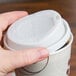 A hand using a Solo white hot cup lid on a coffee cup.