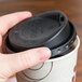 A hand putting a Solo black hot cup lid on a coffee cup.