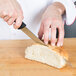 A person using a Mercer Millennia curved bread knife to slice bread.