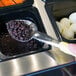 A Vollrath Jacob's Pride perforated basting spoon with a yellow handle scooping black beans into a container.