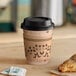 A Choice 12 oz. Kraft paper hot cup with a black lid and a pastry on a table.