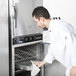 A man in a white coat putting food in an Alto-Shaam smoker oven.