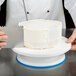 A person using an Ateco plastic cake turntable to cut a white cake.