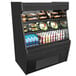 A black Structural Concepts Oasis air curtain merchandiser with food and drinks on shelves.
