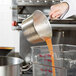 A hand pours orange juice into a Town tapered aluminum sauce pan.