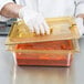 A person in gloves holding a Carlisle amber high heat plastic food pan filled with red sauce.