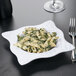 A white square melamine bowl filled with pasta and broccoli with a fork.
